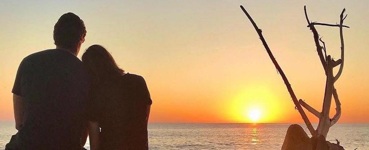 West Coast Couple sitting on tree watching sunset over Pacific Ocean
